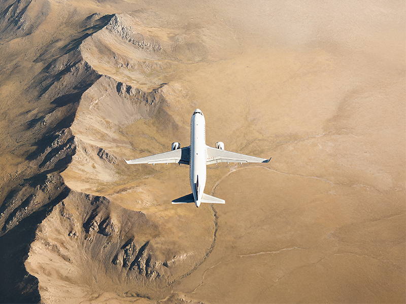 Avoid loss of tracking with ACARS in OpsControl Top-down view of a commercial jet flying over a rugged, sandy landscape, highlighting the aircraft’s wingspan and clean white fuselage.