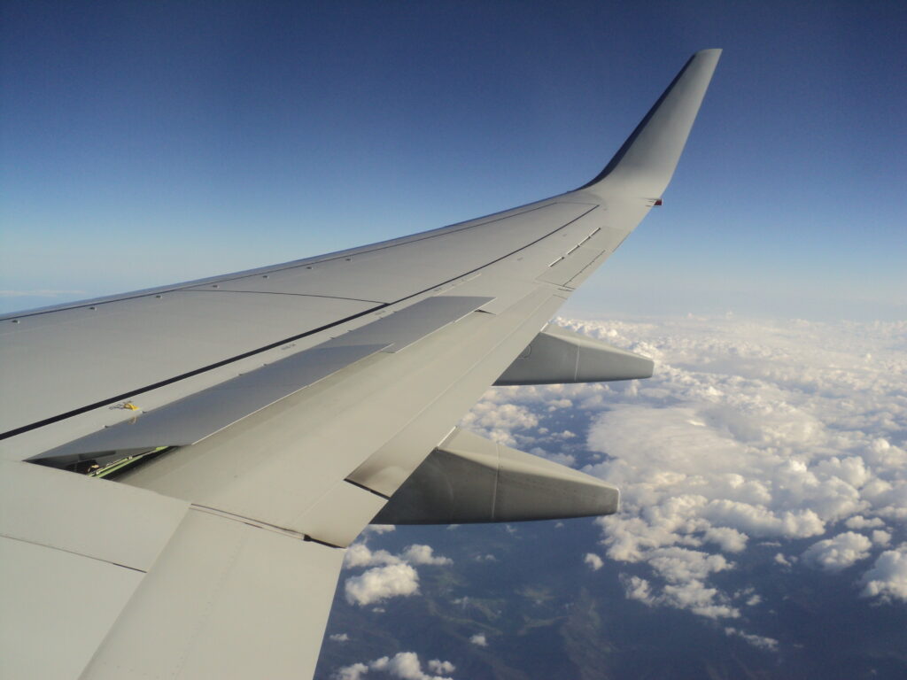 View from an aircraft wing in cruise above scattered clouds, representing efficient flight profiles, reduced fuel burn, and optimized CCO/CDO operations.